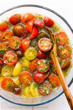 a glass bowl filled with tomatoes and other vegetables, next to a wooden utensil