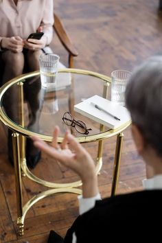 two people sitting at a table with glasses on it and one person holding a cell phone