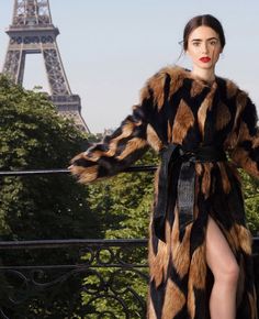 a woman standing in front of the eiffel tower wearing a long fur coat