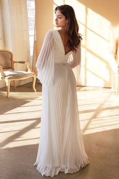 a woman in a white dress is standing near a window and looking off to the side