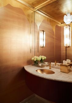 a bathroom with gold walls and marble counter top, two vases on the sink