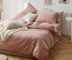 an unmade bed with pink sheets and pillows on top of it in a bedroom