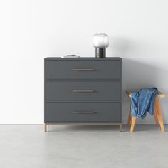 a grey dresser next to a white wall with a blue blanket on it and a wooden stool