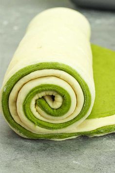 rolled up green and white food item sitting on top of a gray countertop next to a bowl