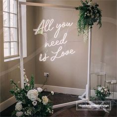 a wedding arch with white flowers and greenery on it that says all you need is love