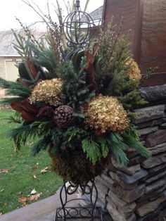 a vase filled with flowers and greenery on top of a metal stand next to a stone wall