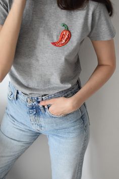 a woman wearing jeans and a t - shirt with a red pepper embroidered on it