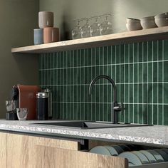 a kitchen with green tiled walls and counter tops, wine glasses on the shelf above the sink