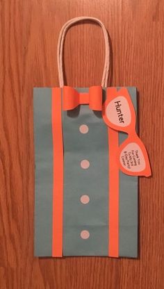 a paper bag with an orange ribbon on it and a tag attached to the handle