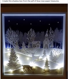 an illuminated window with christmas trees and reindeers in the snow, on display at night