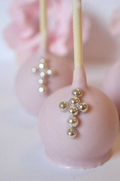 three cake pops with pearls on them sitting next to pink flowers and one has a cross on it