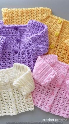 four crocheted sweaters in different colors and sizes are shown on the table