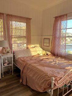 a bed sitting in a bedroom next to two windows with pink drapes on them