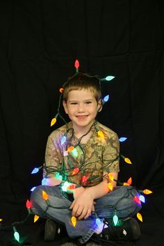 a young boy sitting on the ground with christmas lights all over his body and head