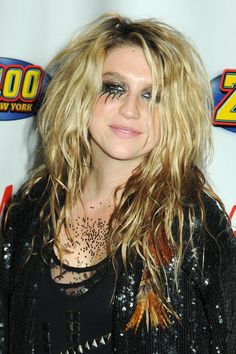 a woman with long blonde hair and black makeup posing for a photo in front of a red carpet