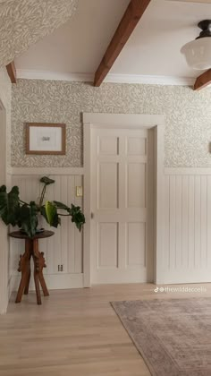 a room with white walls and wooden floors, two plants on a table in front of the door