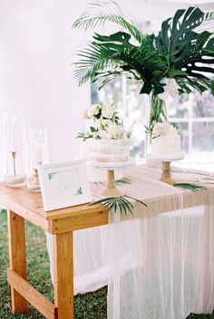 a wooden table topped with a cake next to a potted plant and greenery