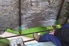 a man sitting on top of a metal bench next to a stone wall and green grass