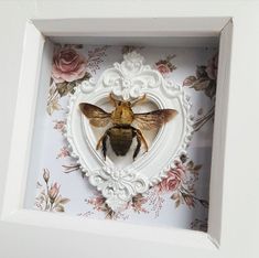 a bee in a heart shaped frame with flowers on the wall and behind it are roses