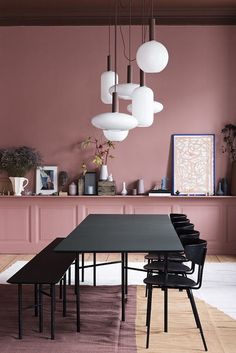 a dining room with pink walls and black table in the center, hanging lights above it