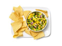 a white plate topped with corn and tortilla chips next to a bowl of salsa