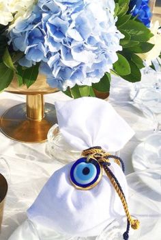 a table topped with blue and white flowers next to an evil eye napkin holder on top of a plate