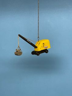 a yellow forklift is suspended from a chain on a light blue background with a pair of scissors