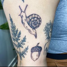 a woman's arm with tattoos on it and an image of a snail, acorns and leaves