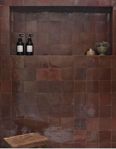 a brown tiled shower with two bottles on the shelf