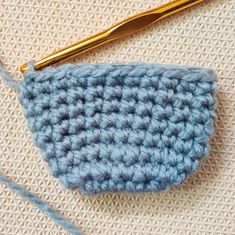 a crocheted blue bag sitting on top of a table next to a knitting needle