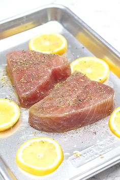 two pieces of raw meat sitting on top of a pan covered in lemons and seasoning