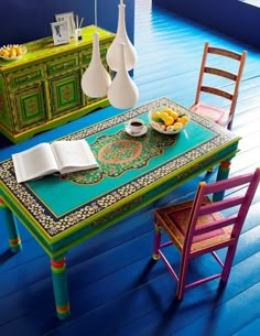 a dining room with blue flooring and colorful furniture on the wooden table, next to a bowl of fruit