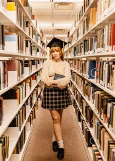 a woman standing in front of a library full of books wearing a graduation cap and plaid skirt