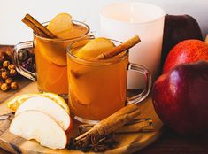 two mugs filled with apple cider and cinnamon on top of a cutting board