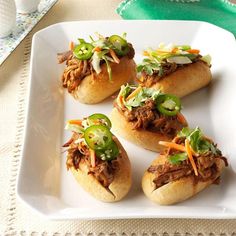 four pulled pork sandwiches on a white plate with green peppers and shredded carrots in the middle