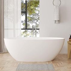 a large white bath tub sitting on top of a wooden floor next to a window