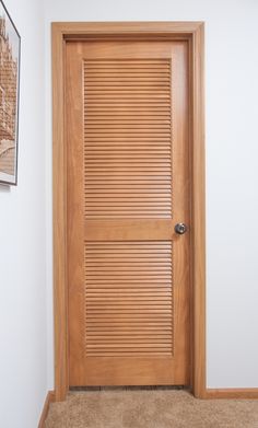 a wooden door with slats on it in a white walled room next to a carpeted floor