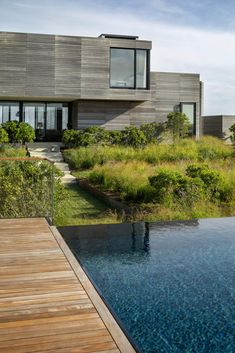 a wooden deck next to a swimming pool in front of a large house with an ocean view