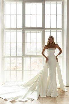 a woman standing in front of a window wearing a white wedding dress with long train