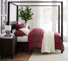 a bedroom decorated for christmas with red and green plaid bedding, pine tree in the corner