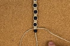 someone is making a bracelet out of black beads and white thread on the ground with their hand