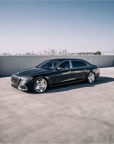 a black car parked on top of a parking lot next to a tall building with a city skyline in the background