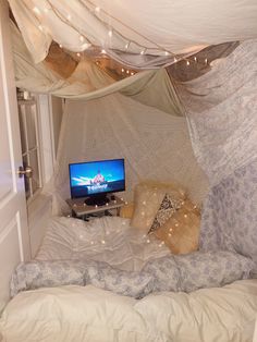 a tv sitting on top of a bed in a room with curtains and lights hanging from the ceiling