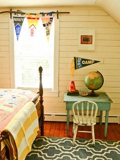 a bedroom with a bed, desk and chair next to a window that has flags on it