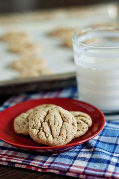 two cookies are on a red plate next to a glass of milk and a plaid cloth