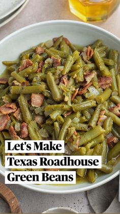 a bowl filled with green beans and bacon next to two silver spoons on a table