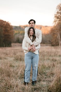 a man and woman standing in the middle of a field with their arms around each other