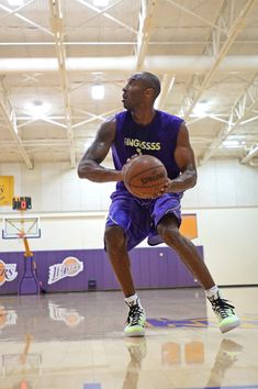 a man in purple jersey holding a basketball on a court with other people watching from the sidelines