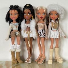 four dolls are lined up in front of each other on a shelf, one is wearing white and the other has black hair