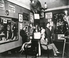 an old black and white photo of people in a room with pictures on the walls